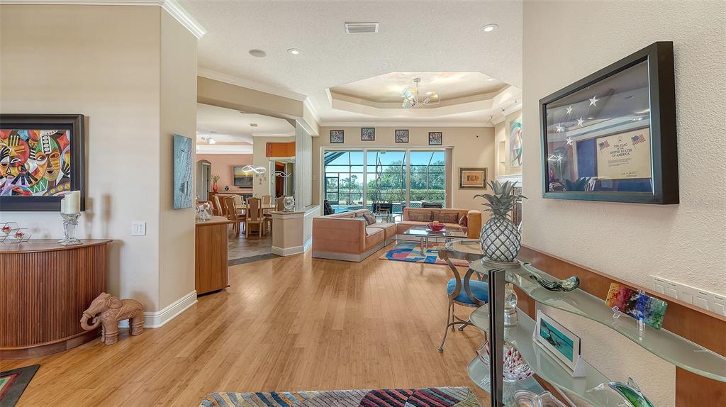 A bright living room with hardwood floors, a tray ceiling, and a view of the pool — 7522 CONSERVATION COURT, SARASOTA, FL