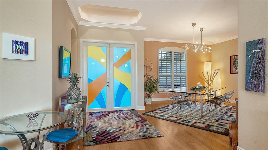 A bright entryway and dining room feature colorful glass double doors and a glass table — 7522 CONSERVATION COURT, SARASOTA, FL