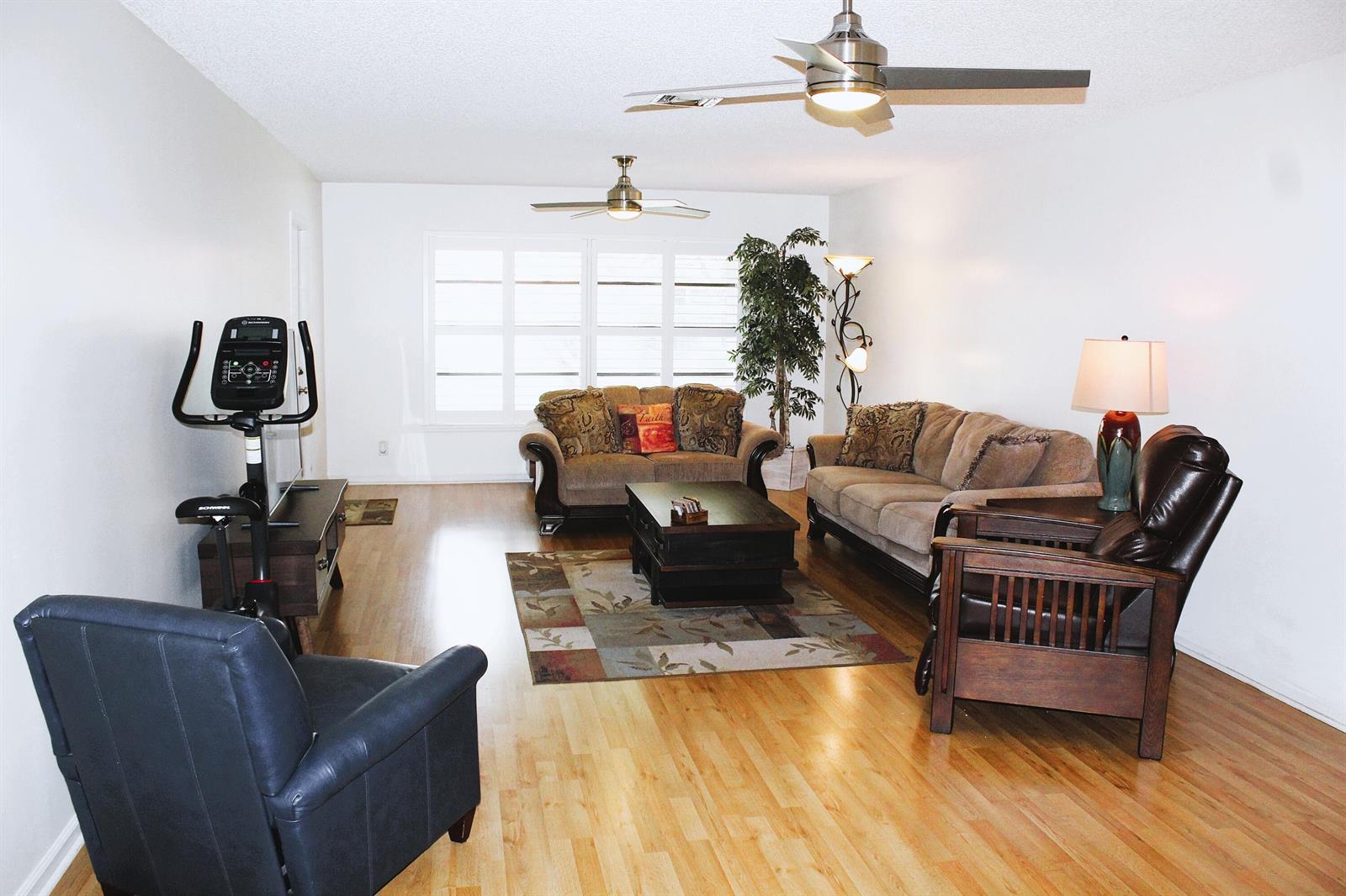 A living room features hardwood floors, two ceiling fans, a stationary bike, and neutral furniture — 4525 Nutmeg Tree Lane # A, Boynton Beach FL 33436, BOYNTON BEACH, FL