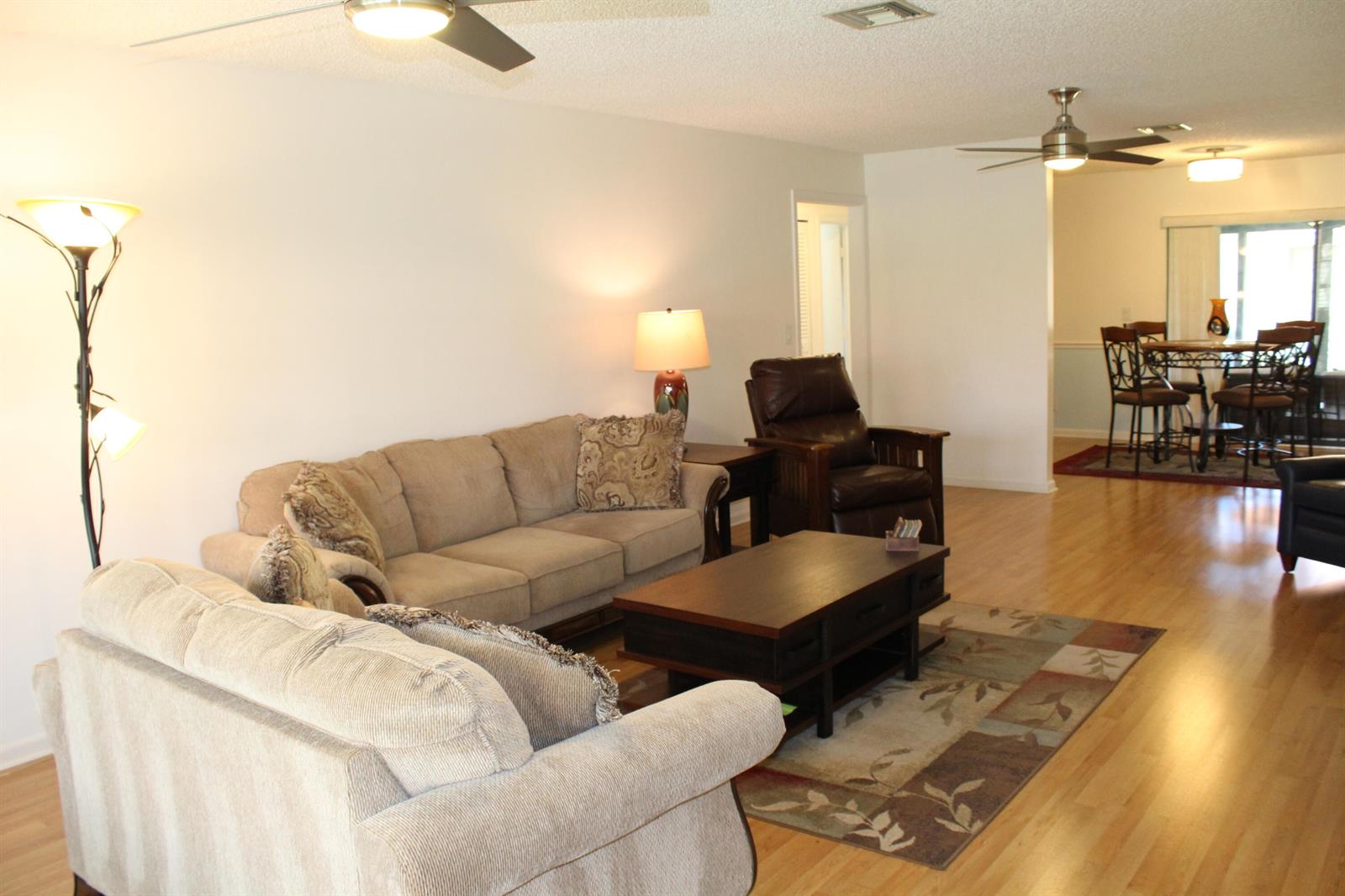 A living room with light-colored sofas, a dark wood coffee table, and hardwood flooring — 4525 Nutmeg Tree Lane # A, Boynton Beach FL 33436, BOYNTON BEACH, FL