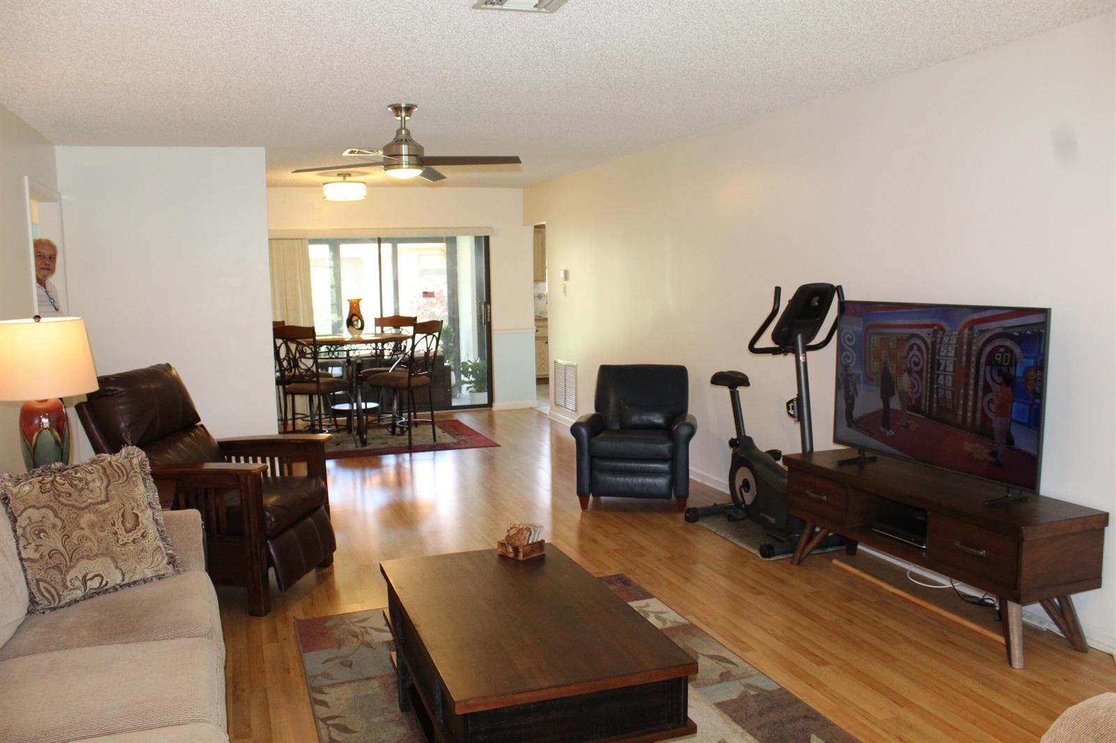 A living room with hardwood floors, a television, exercise bike, and an adjacent dining area — 4525 Nutmeg Tree Lane # A, Boynton Beach FL 33436, BOYNTON BEACH, FL