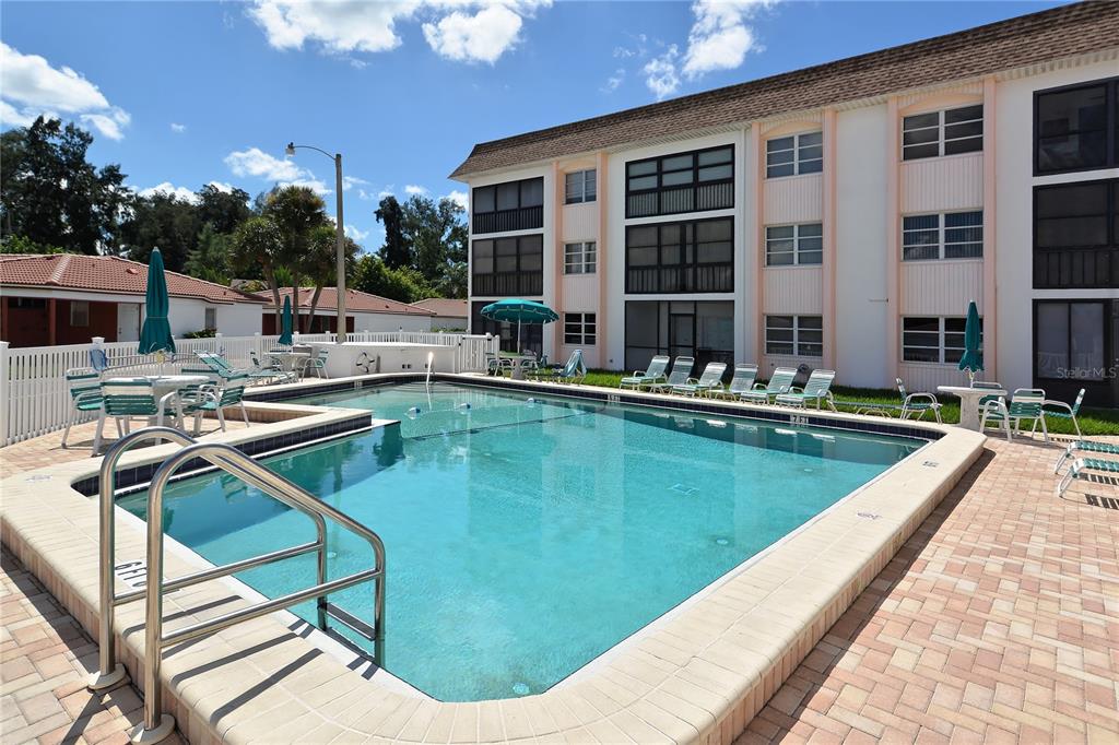 A swimming pool with lounge chairs and tables sits in front of a multi-story apartment building — 116 VISTA HERMOSA CIRCLE UNIT 308C, SARASOTA, FL
