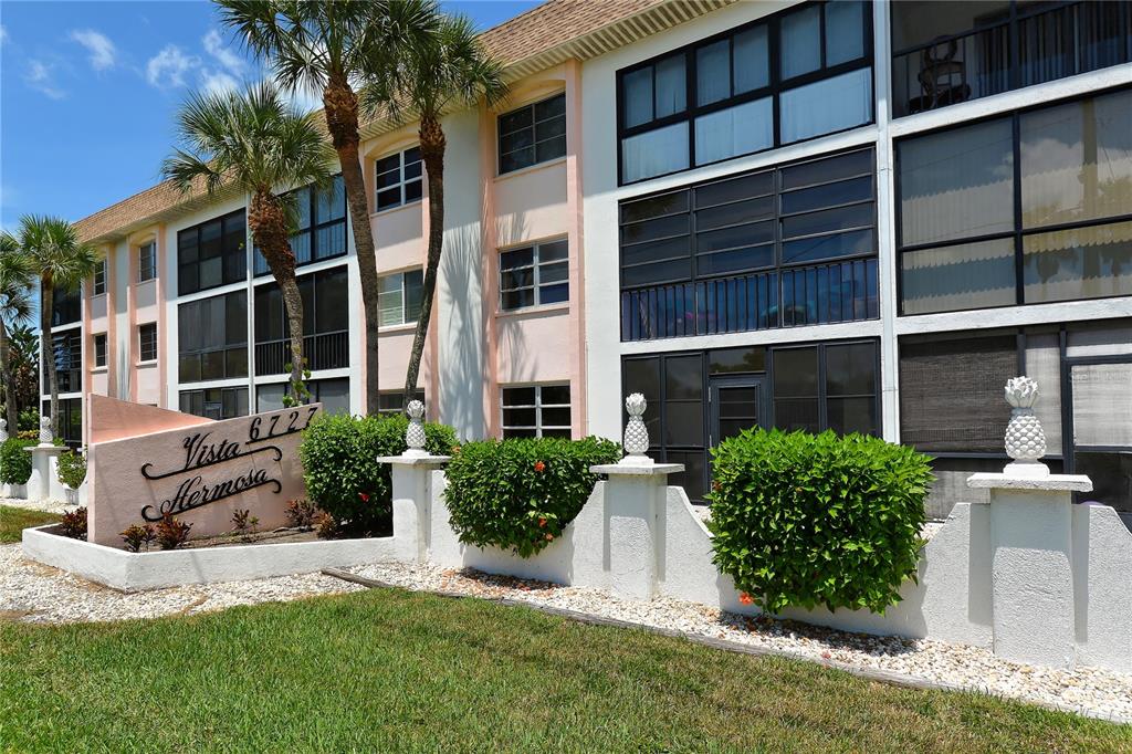 The exterior of a multi-story apartment building features a sign and decorative pineapple finials — 116 VISTA HERMOSA CIRCLE UNIT 308C, SARASOTA, FL