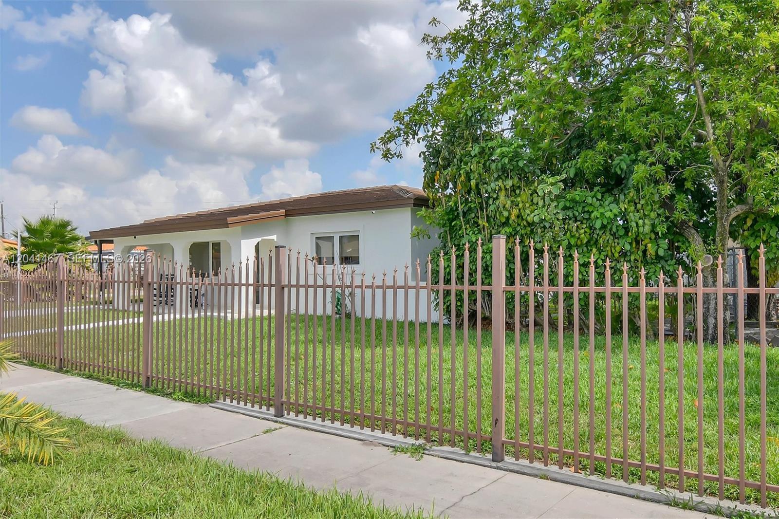 A white single-story house is viewed from the street behind a tall metal fence — 241 W 48th St, Hialeah FL 33012, HIALEAH, FL