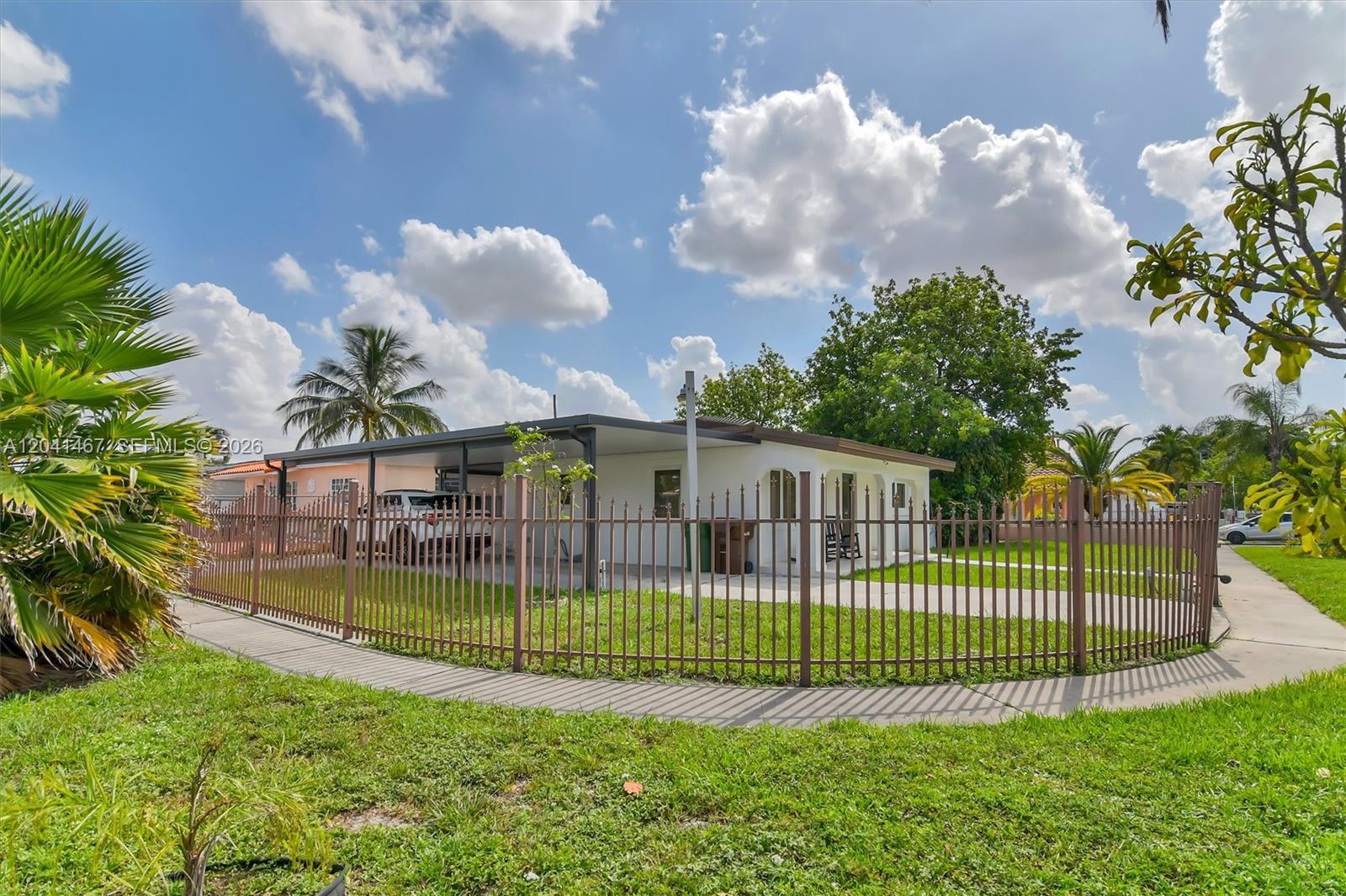 A single-story house with a carport is enclosed by a metal fence on a lawn — 241 W 48th St, Hialeah FL 33012, HIALEAH, FL