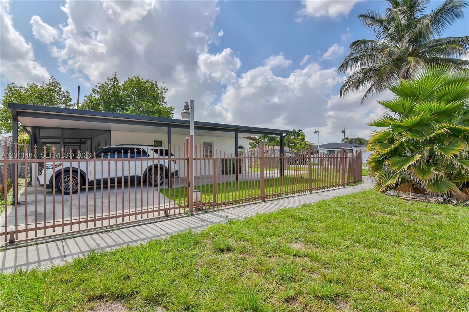 A white SUV is parked under a carport behind a metal fence on a sunny day — 241 W 48th St, Hialeah FL 33012, HIALEAH, FL
