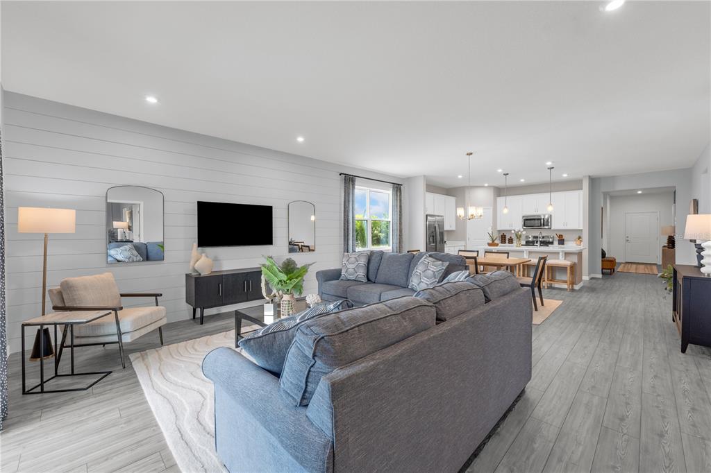 An open-concept living room features gray wood-look flooring, a shiplap accent wall, and a kitchen — 3836 RISING TRAIL, DAVENPORT, FL