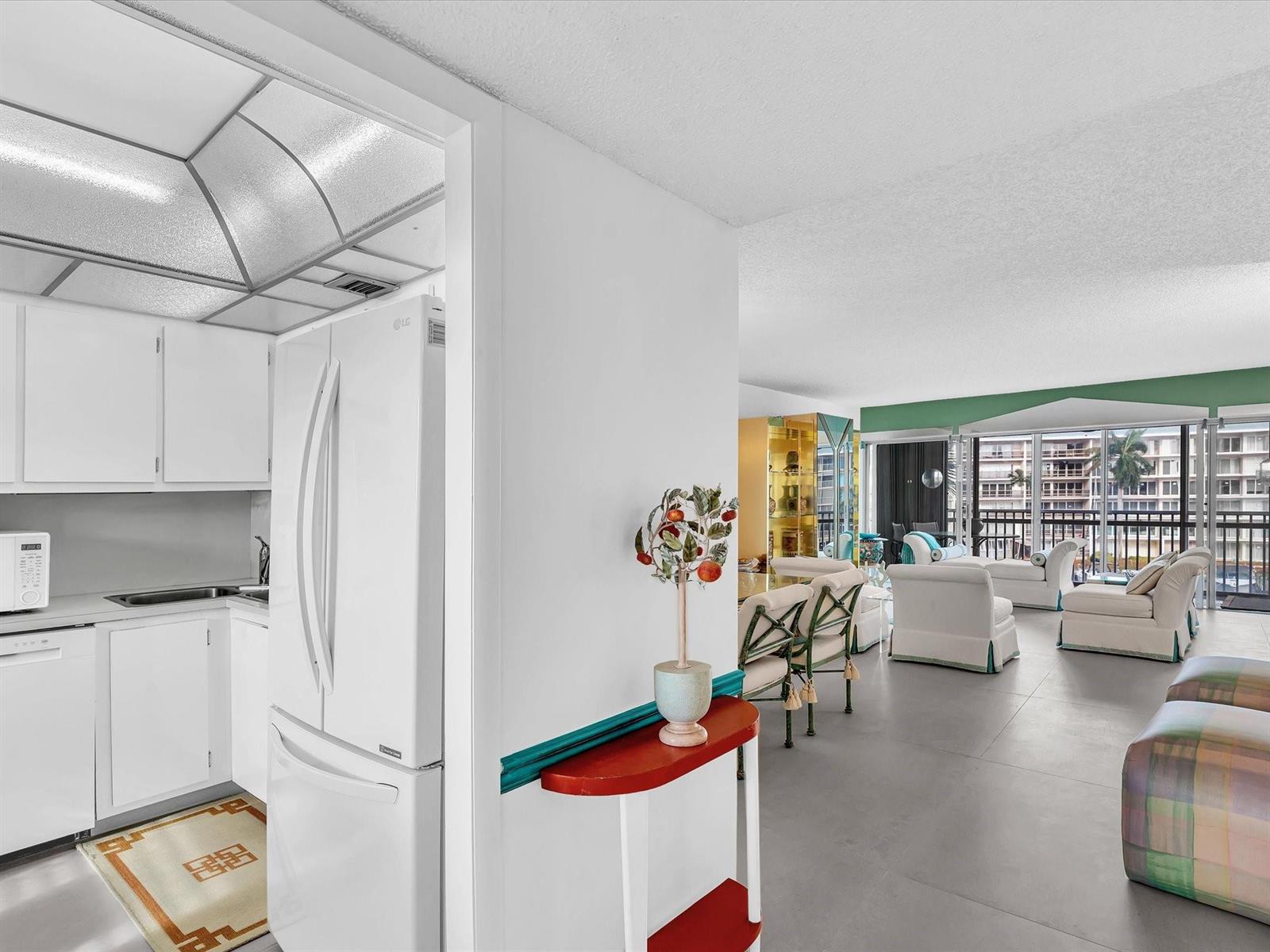 A white kitchen with a refrigerator opens into a bright living area with balcony views — 1537 E Hillsboro Boulevard # 438, Deerfield Beach FL 33441, DEERFIELD BEACH, FL