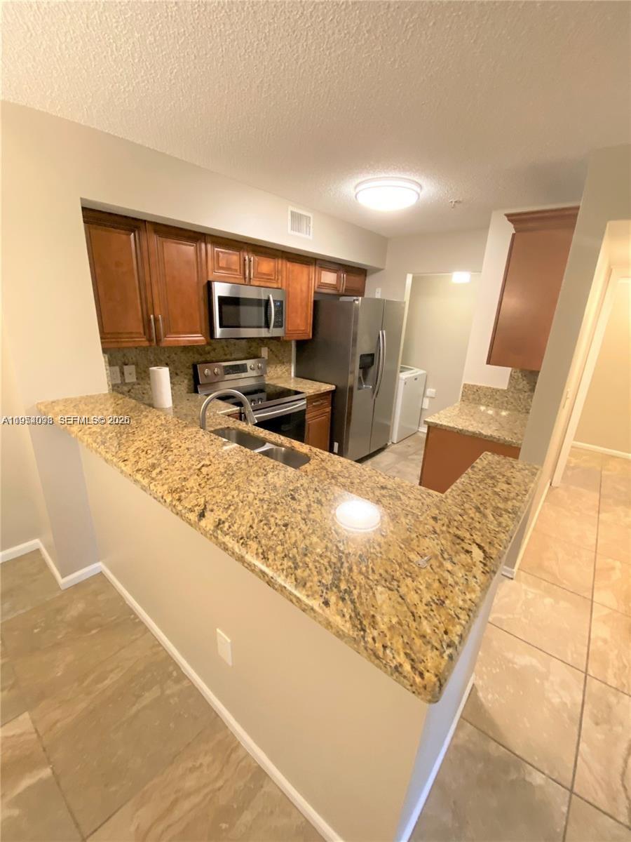 This kitchen features wood cabinets, granite countertops, stainless steel appliances, and a breakfast bar — 2133 Renaissance Blvd # 306, Miramar FL 33025, MIRAMAR, FL