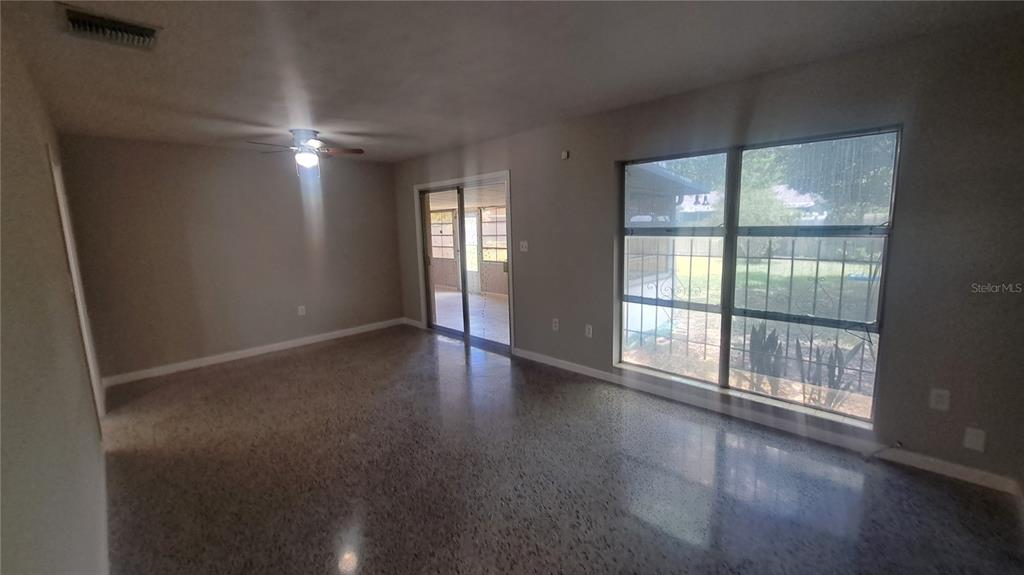 An empty living room features polished terrazzo floors, a ceiling fan, and large windows — 5329 SATEL DRIVE, ORLANDO, FL