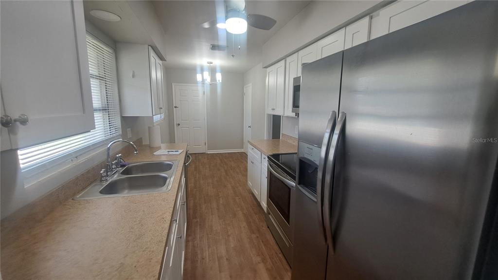 A kitchen features white cabinets, tan countertops, stainless steel appliances, and wood-look flooring — 5329 SATEL DRIVE, ORLANDO, FL