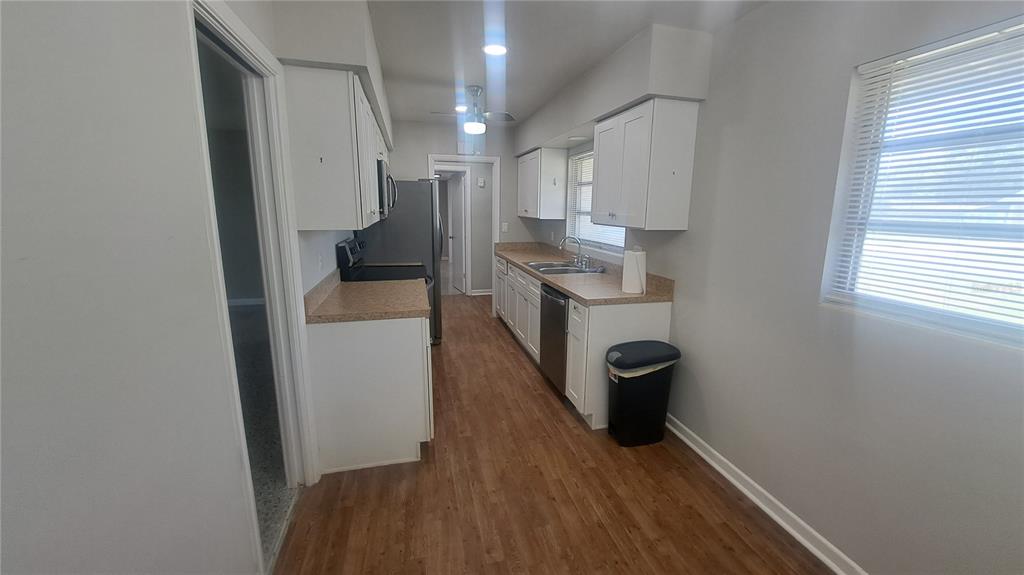 A galley-style kitchen features white cabinets, laminate countertops, stainless steel appliances, and wood-look flooring — 5329 SATEL DRIVE, ORLANDO, FL