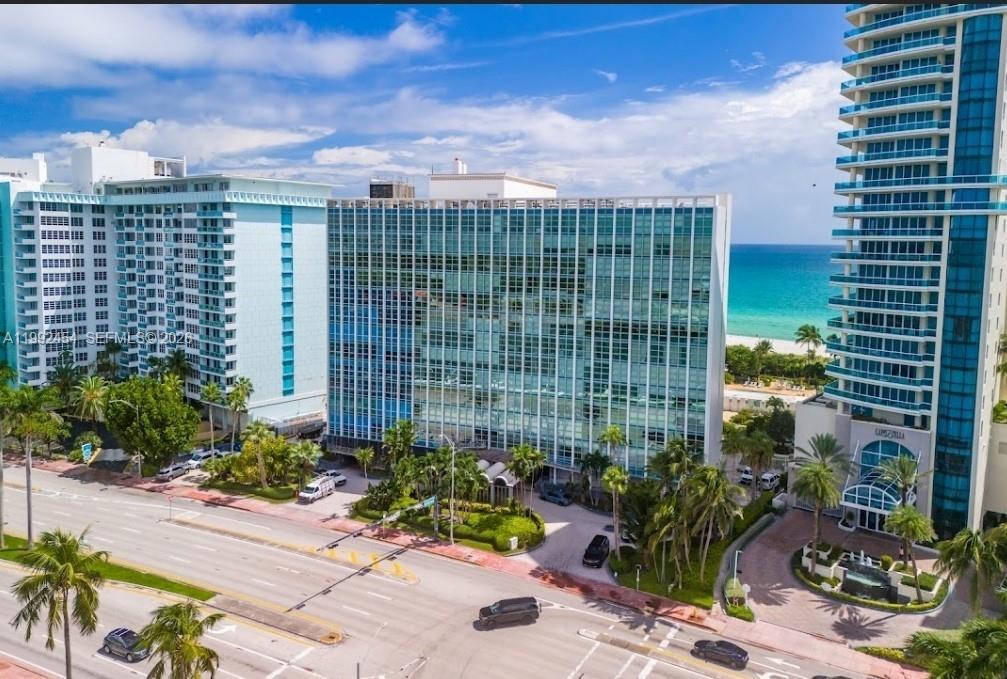 An aerial view of a glass-facade apartment building situated between two high-rise towers near the ocean — 5055 Collins Ave # 2K, Miami Beach FL 33140, MIAMI BEACH, FL