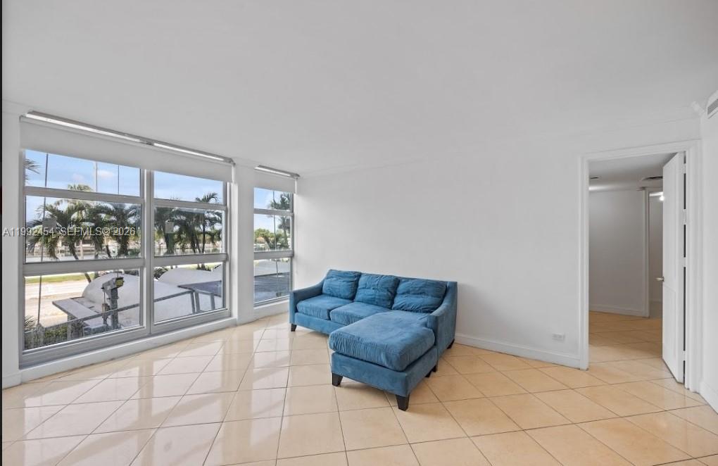 A living room with beige tile floors, a blue sectional sofa, and large windows — 5055 Collins Ave # 2K, Miami Beach FL 33140, MIAMI BEACH, FL