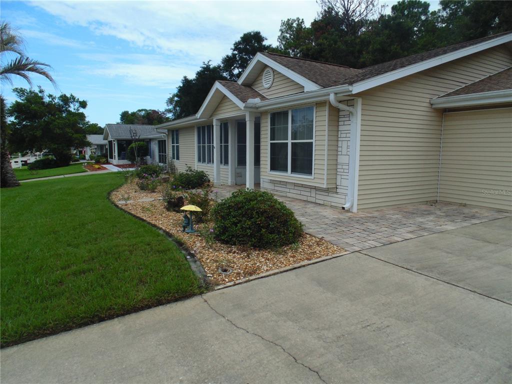 A tan vinyl-sided house features a paved walkway, a landscaped garden bed, and a concrete driveway — 8125 SW 108 LOOP, OCALA, FL