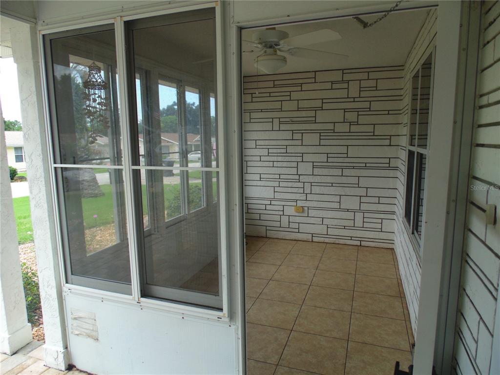 A screened-in porch features tiled flooring, a ceiling fan, and white stone-patterned wall panels — 8125 SW 108 LOOP, OCALA, FL