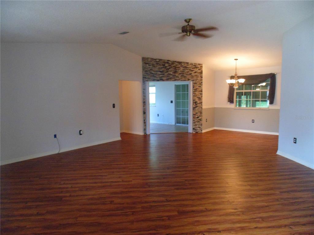 An open living area features wood-look flooring, a stone accent wall, and a ceiling fan — 8125 SW 108 LOOP, OCALA, FL