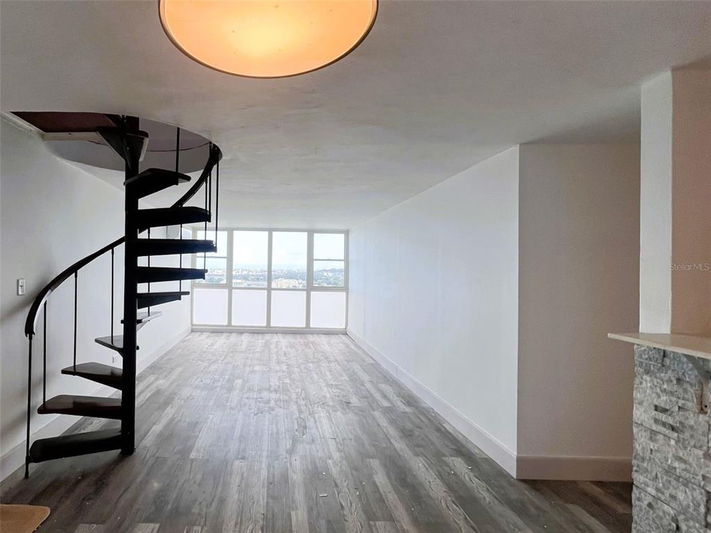 An empty room features wood-look flooring, white walls, a spiral staircase, and large windows — 1812 ALCALA UNIT 2301, SAN JUAN, PR