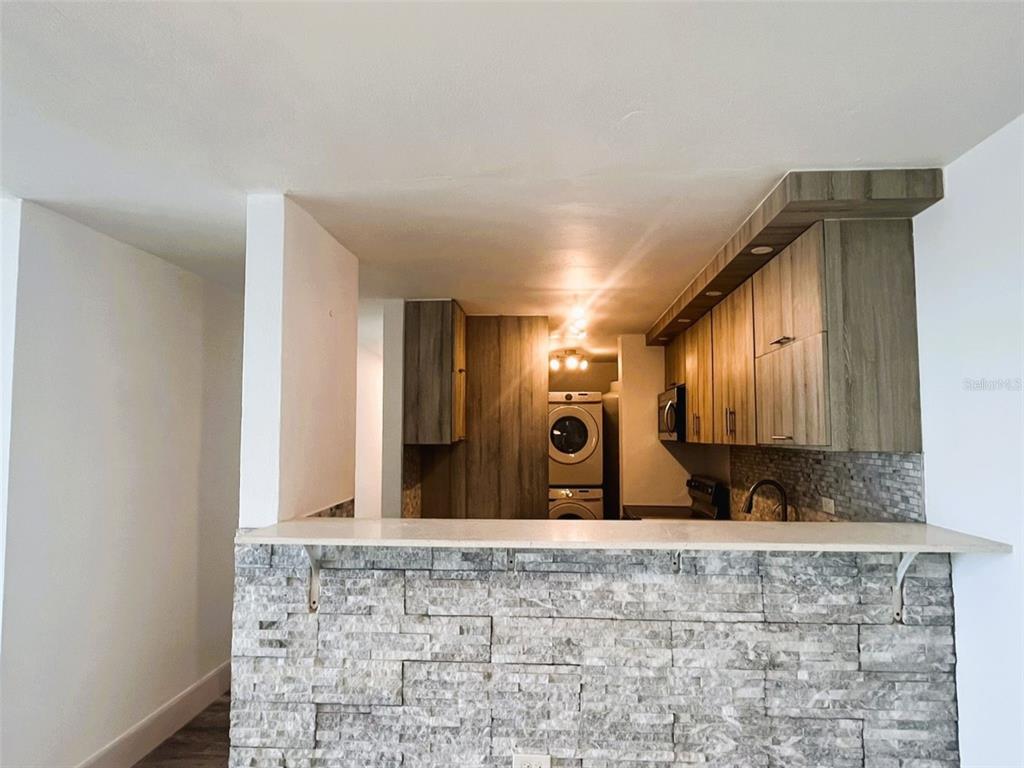 A kitchen features wood-toned cabinets, a stone-tiled breakfast bar, and a stacked washer and dryer — 1812 ALCALA UNIT 2301, SAN JUAN, PR