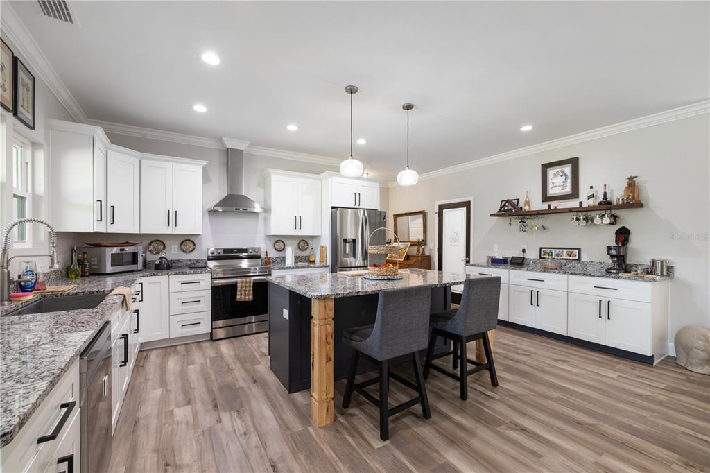 A kitchen features white cabinets, granite countertops, a dark island with bar stools, and stainless appliances — 5149 SW 119TH PLACE, LAKE BUTLER, FL