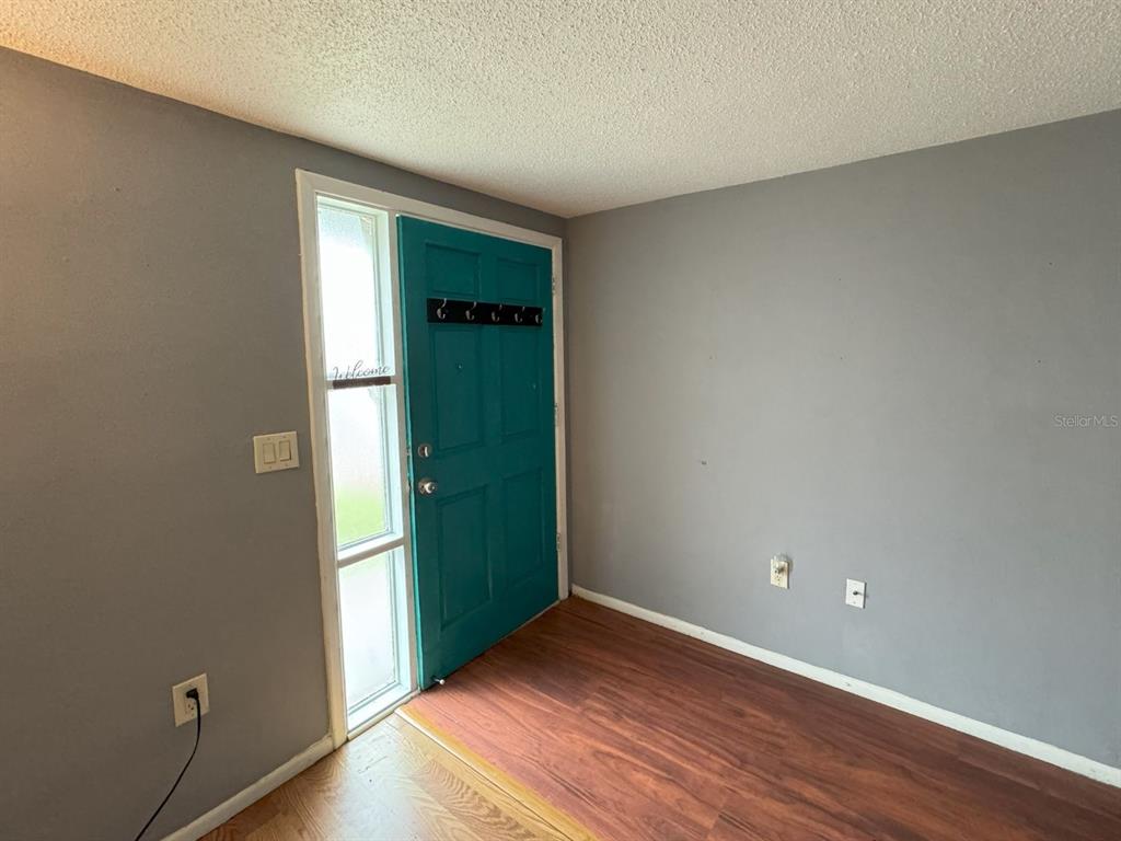 An entryway features a teal front door, gray walls, and wood-look flooring — 7410 CASTANEA DRIVE, PORT RICHEY, FL