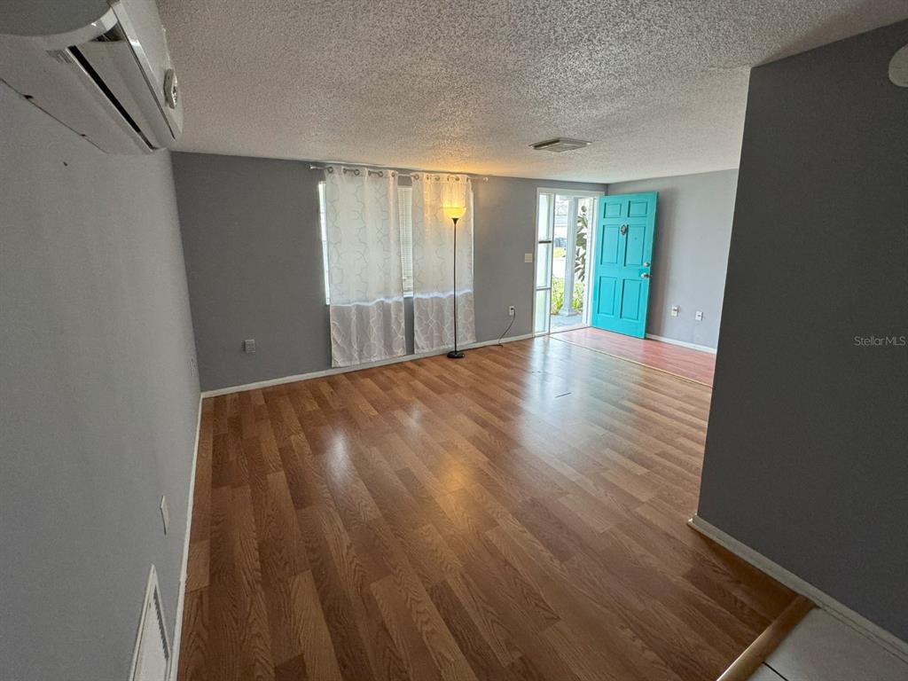An empty living room features gray walls, wood-look flooring, a teal front door, and curtains — 7410 CASTANEA DRIVE, PORT RICHEY, FL