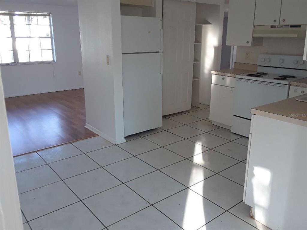 A kitchen with white appliances, white cabinets, and tiled floors leads into a living area — 7410 CASTANEA DRIVE, PORT RICHEY, FL