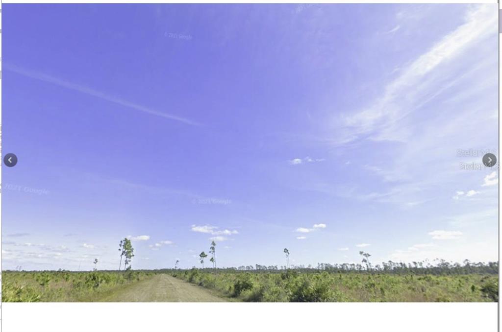 A dirt road stretches through a flat, grassy field under a bright blue sky — CALLIANDRA DRIVE, INDIAN LAKE ESTATES, FL
