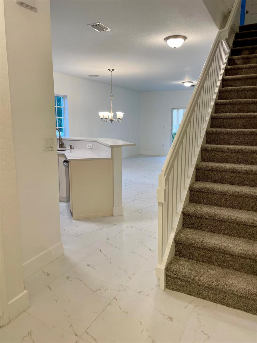 A view of a kitchen with white countertops and a staircase with carpeted steps — 4987 SE Mariner Garden Circle, Stuart FL 34997, STUART, FL