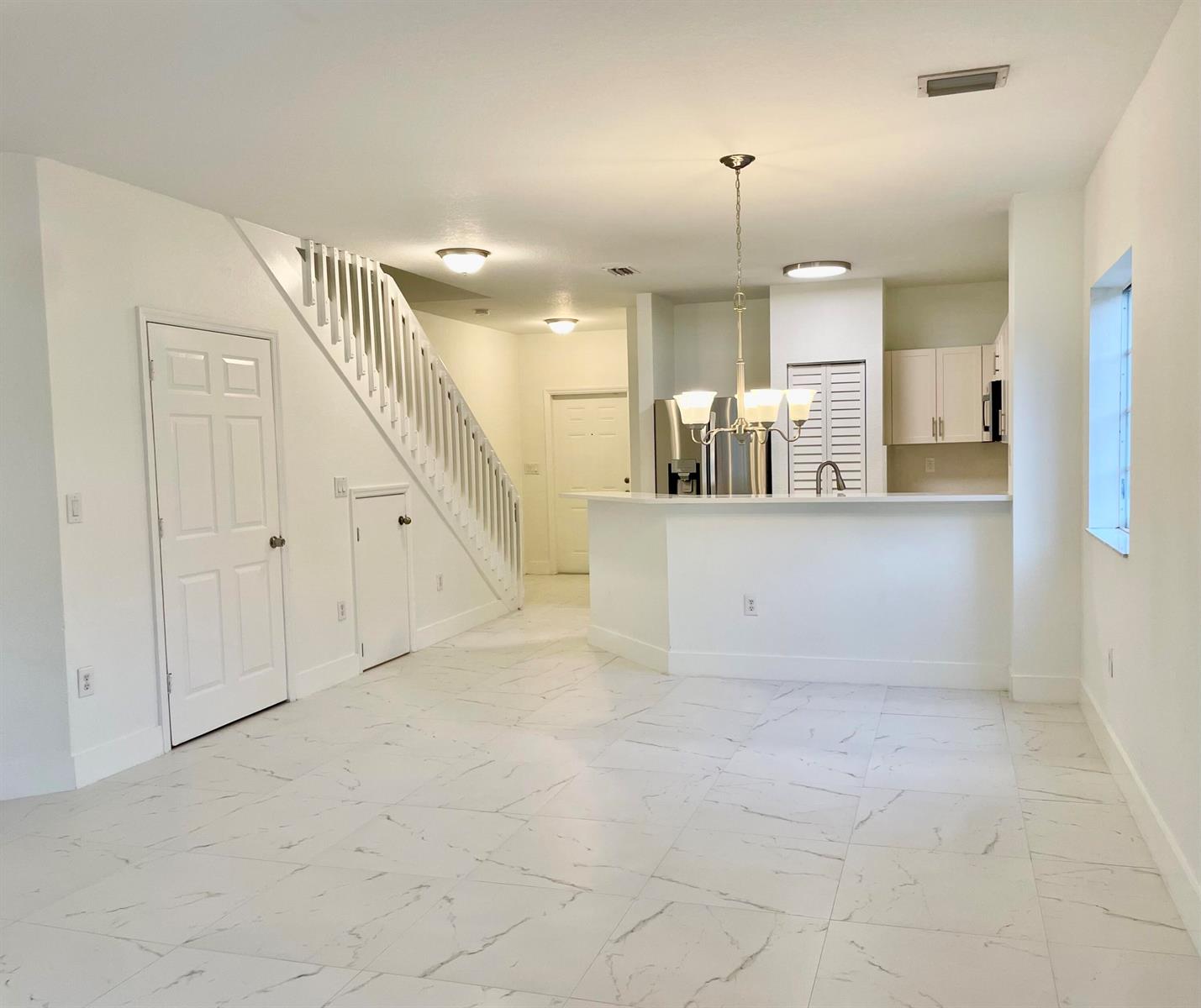 An open-concept room features white tile floors, a staircase, and a kitchen with white cabinets — 4987 SE Mariner Garden Circle, Stuart FL 34997, STUART, FL