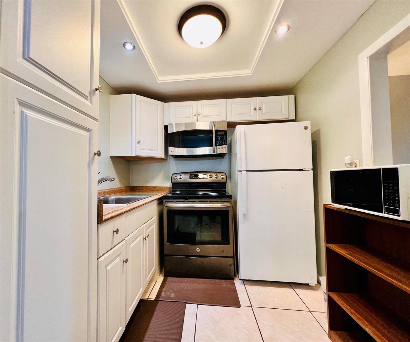 A small kitchen features white cabinets, a dark stove, a white refrigerator, and tiled floors — 330 Southampton B, West Palm Beach FL 33417, WEST PALM BEACH, FL