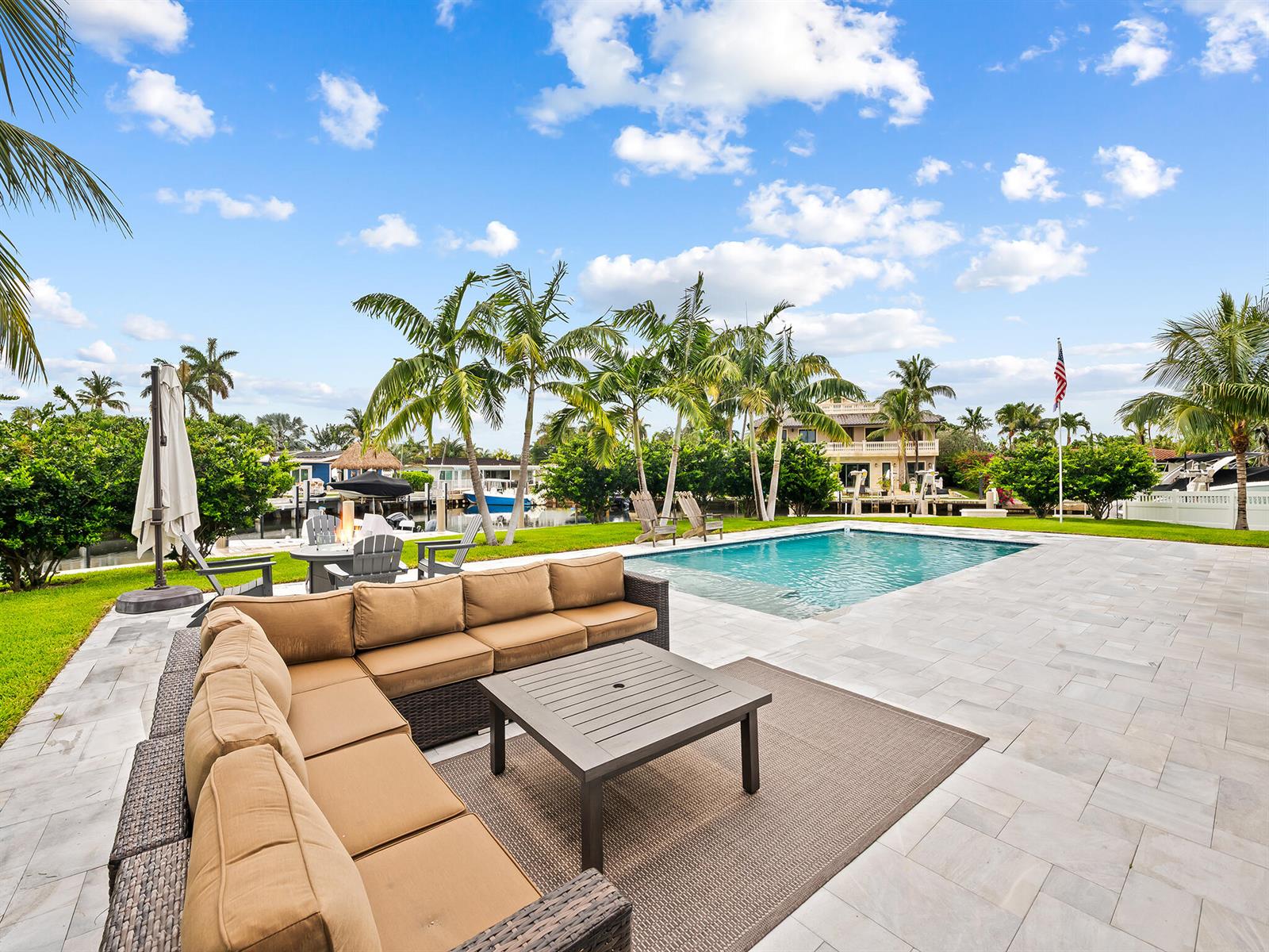 A patio features a sectional sofa, coffee table, swimming pool, and palm trees by water — 2421 NE 50th Street, Lighthouse Point FL 33064, LIGHTHOUSE POINT, FL