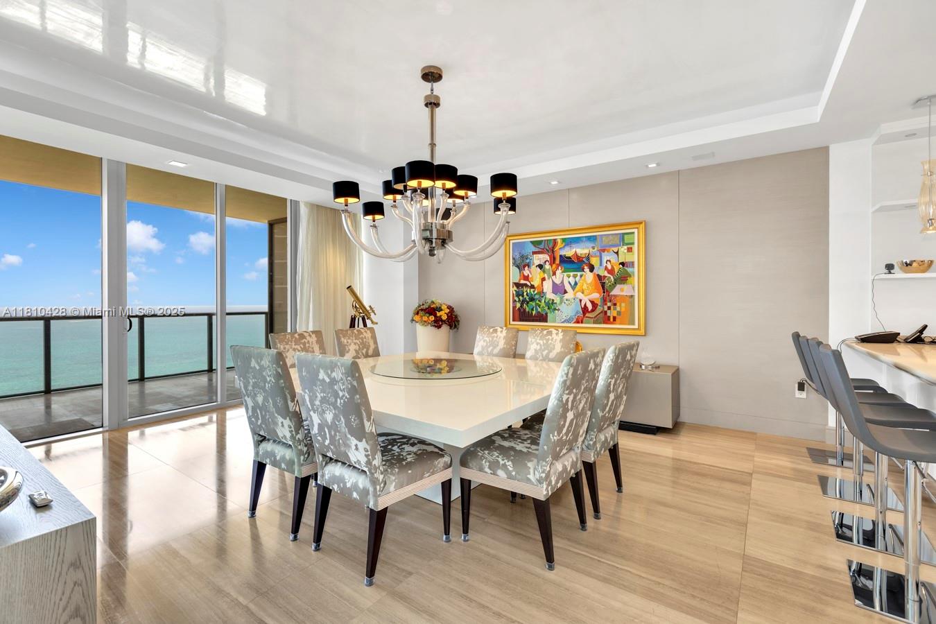 A dining room features a square table, patterned chairs, a chandelier, and an ocean view — 9701 Collins Ave # 2403S, Bal Harbour FL 33154, BAL HARBOUR, FL