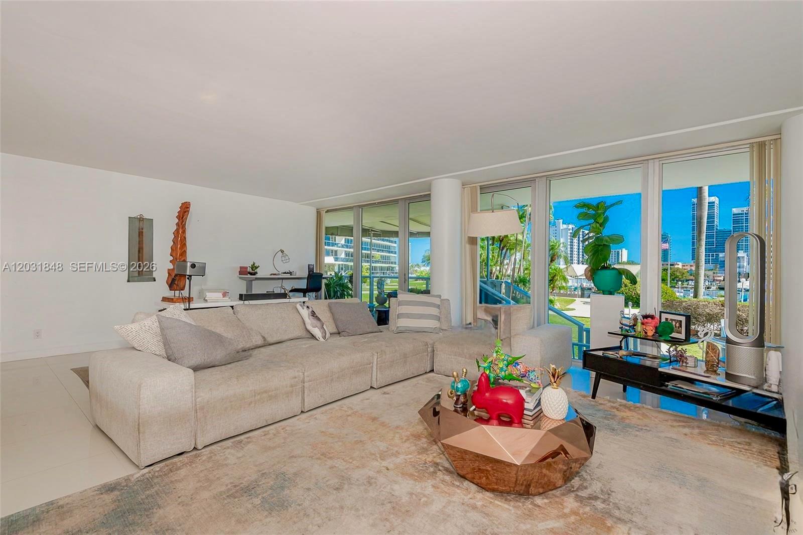 A living room features a large sectional sofa, a geometric coffee table, and floor-to-ceiling windows — 900 Bay Dr # 122, Miami Beach FL 33141, MIAMI BEACH, FL