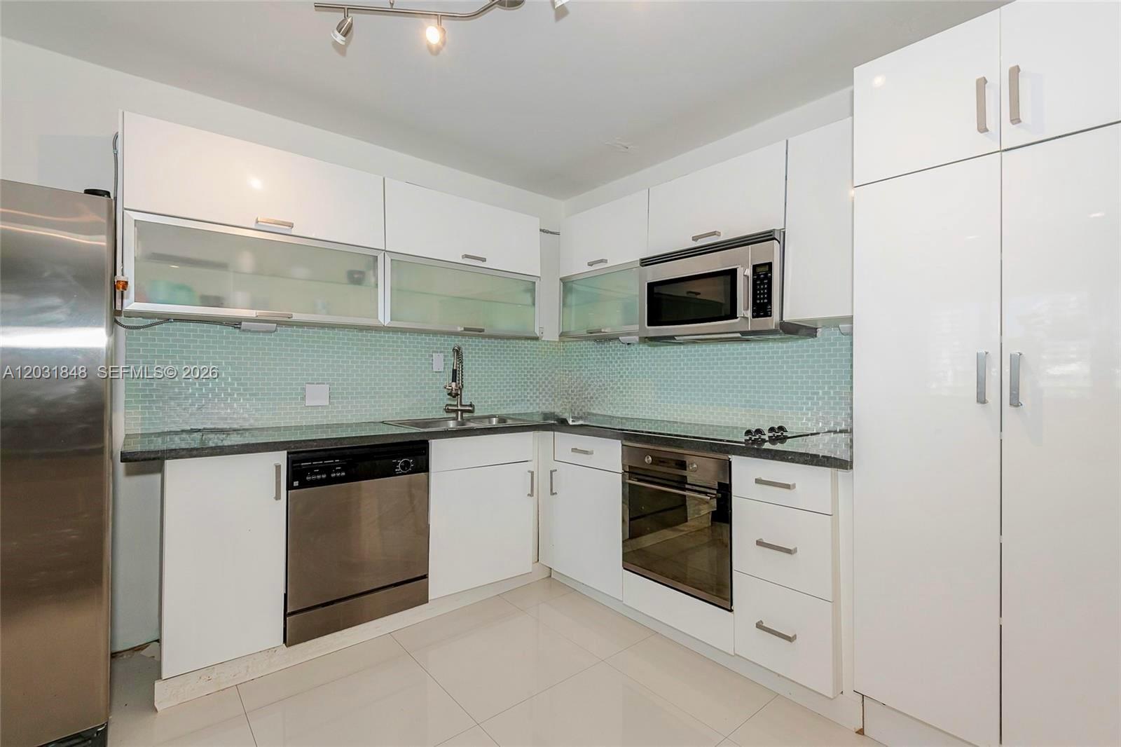 A modern kitchen features white cabinets, stainless steel appliances, and a light blue tiled backsplash — 900 Bay Dr # 122, Miami Beach FL 33141, MIAMI BEACH, FL