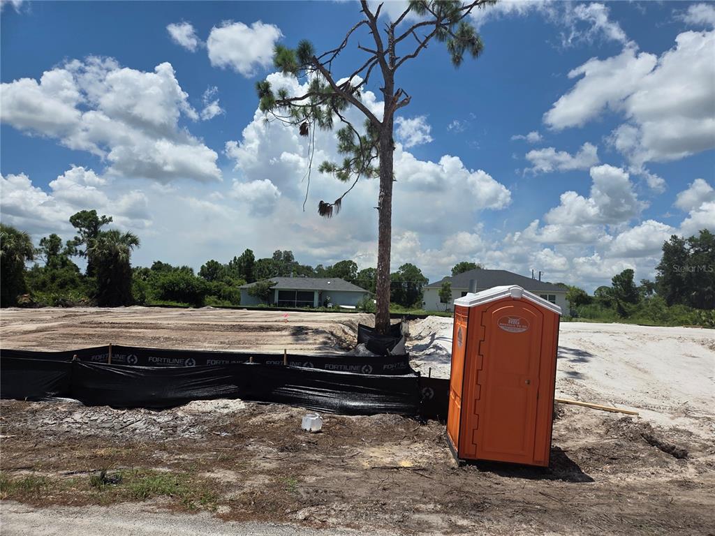 An orange portable toilet sits on a cleared construction lot with a single pine tree — SELOVER ROAD, NORTH PORT, FL
