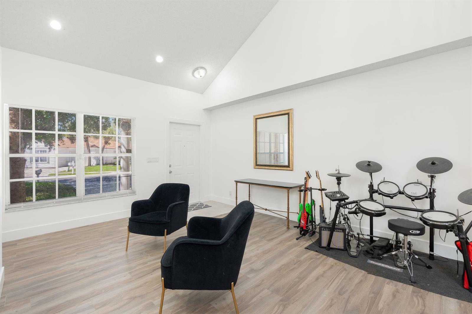 A bright living room features vaulted ceilings, wood-look flooring, two black chairs, and a drum set — 4846 Purdue Drive, Boynton Beach FL 33436, BOYNTON BEACH, FL