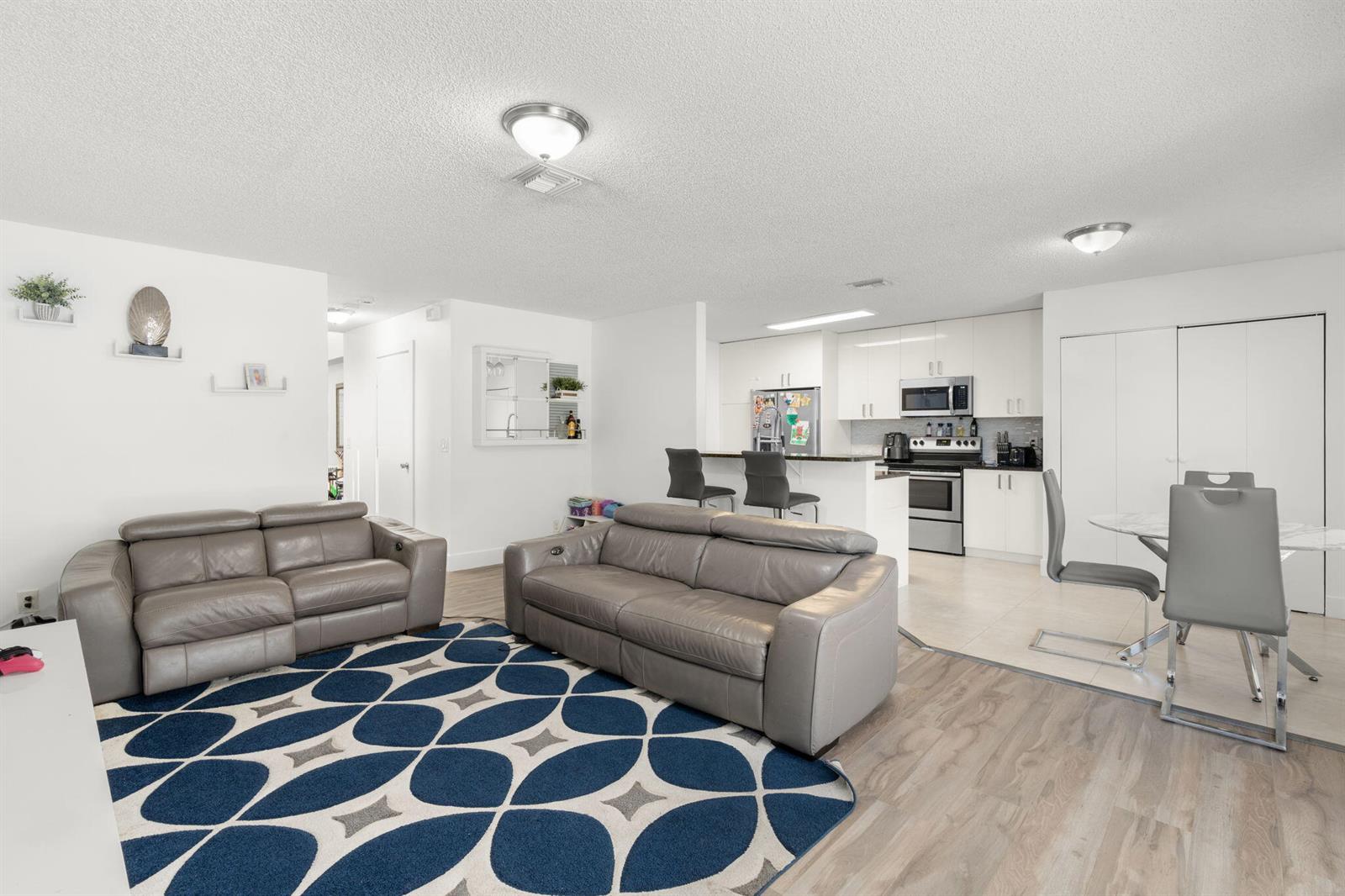 An open-concept living room and kitchen featuring grey leather sofas, a patterned rug, and cabinetry — 4846 Purdue Drive, Boynton Beach FL 33436, BOYNTON BEACH, FL