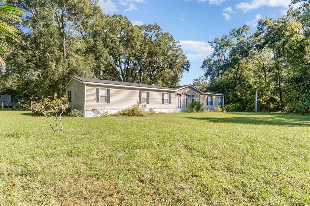 A single-story manufactured home with beige siding sits on a large, grassy lot — 18905 NW 250TH STREET, HIGH SPRINGS, FL
