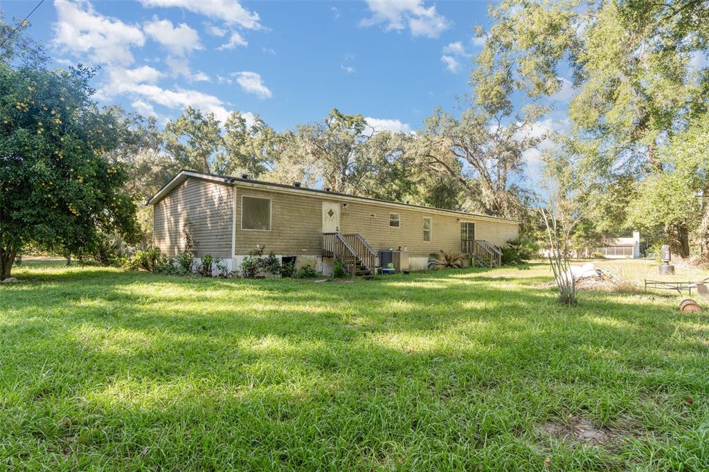 A single-story manufactured home sits on a grassy lot surrounded by mature trees — 18905 NW 250TH STREET, HIGH SPRINGS, FL