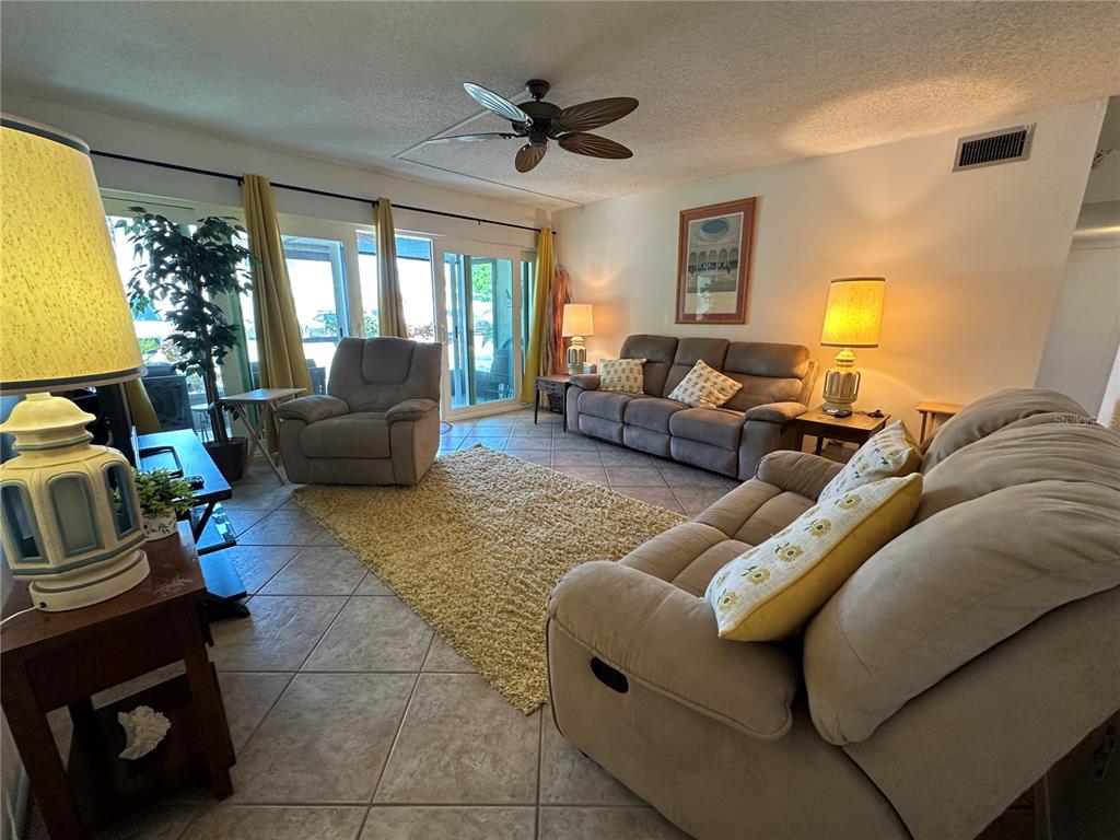 A living room features tile flooring, a shaggy rug, neutral furniture, and sliding glass doors — 2950 CLARK ROAD UNIT 112, SARASOTA, FL