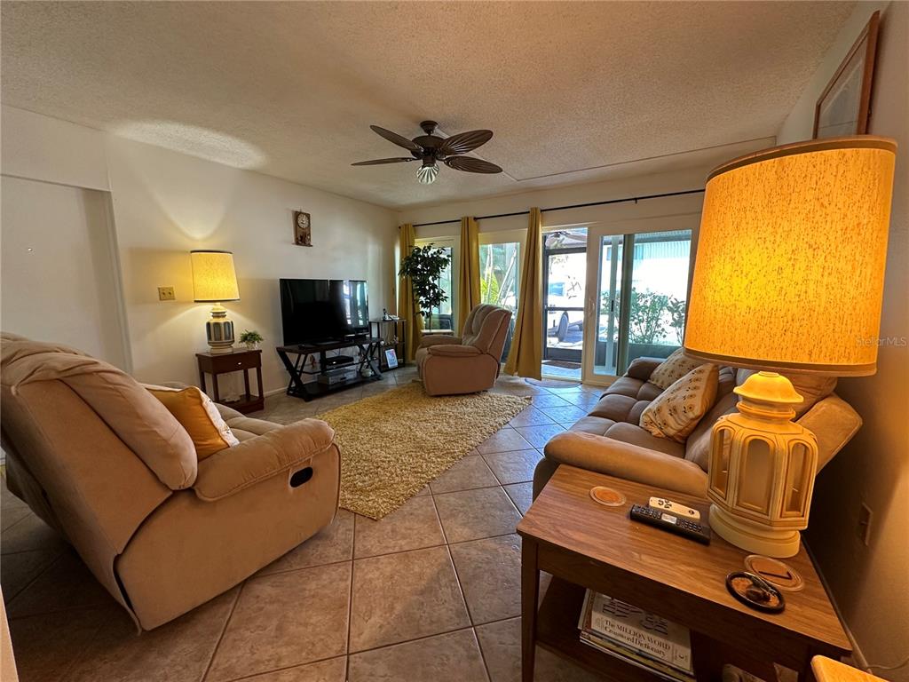 A living room features tile flooring, a ceiling fan, a television, and two beige recliners — 2950 CLARK ROAD UNIT 112, SARASOTA, FL