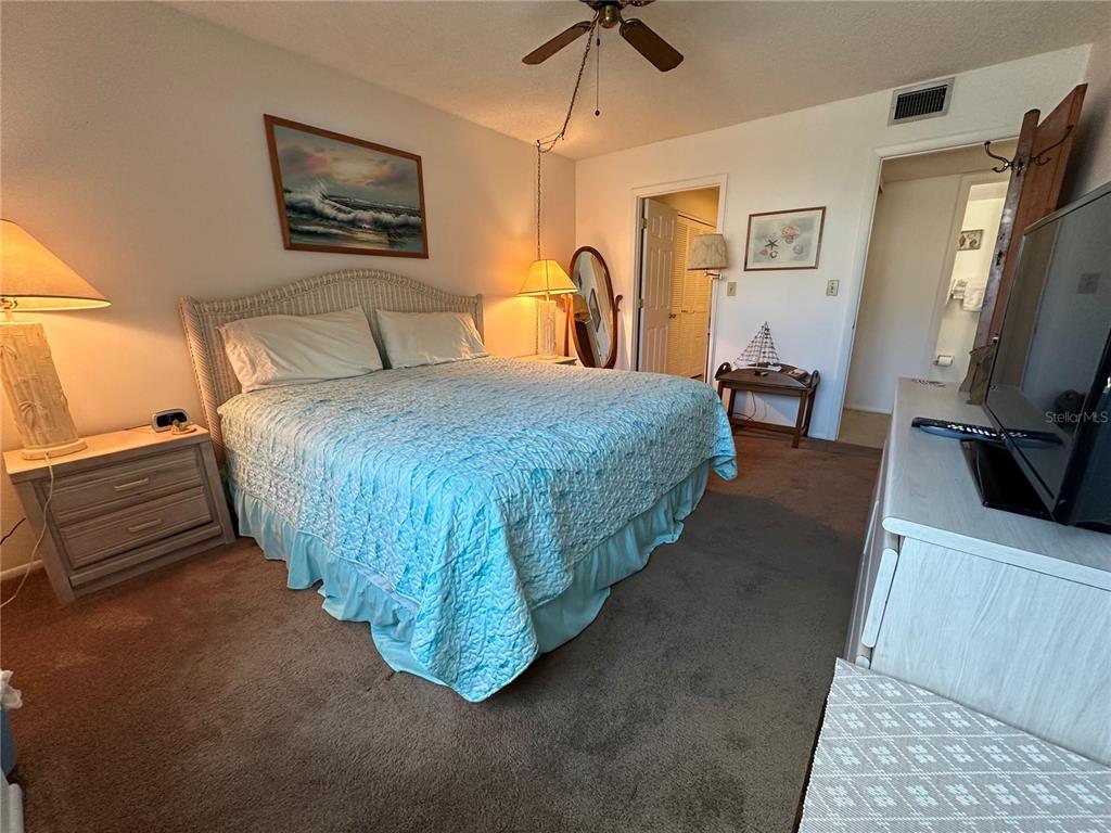 A bedroom features a bed with a blue quilt, two nightstands, and a television — 2950 CLARK ROAD UNIT 112, SARASOTA, FL