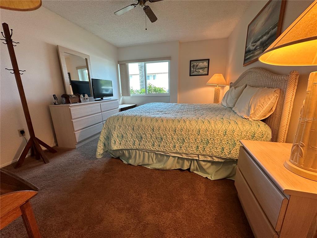 A bedroom features a bed with a wicker headboard, a dresser, and a ceiling fan — 2950 CLARK ROAD UNIT 112, SARASOTA, FL