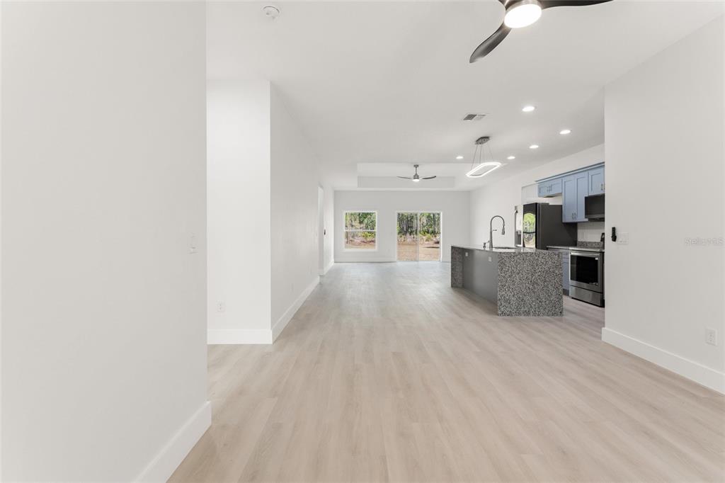An open-concept kitchen and living area features light wood flooring, a granite island, and blue cabinetry — 3750 JAPONICA AVENUE, INDIAN LAKE ESTATES, FL