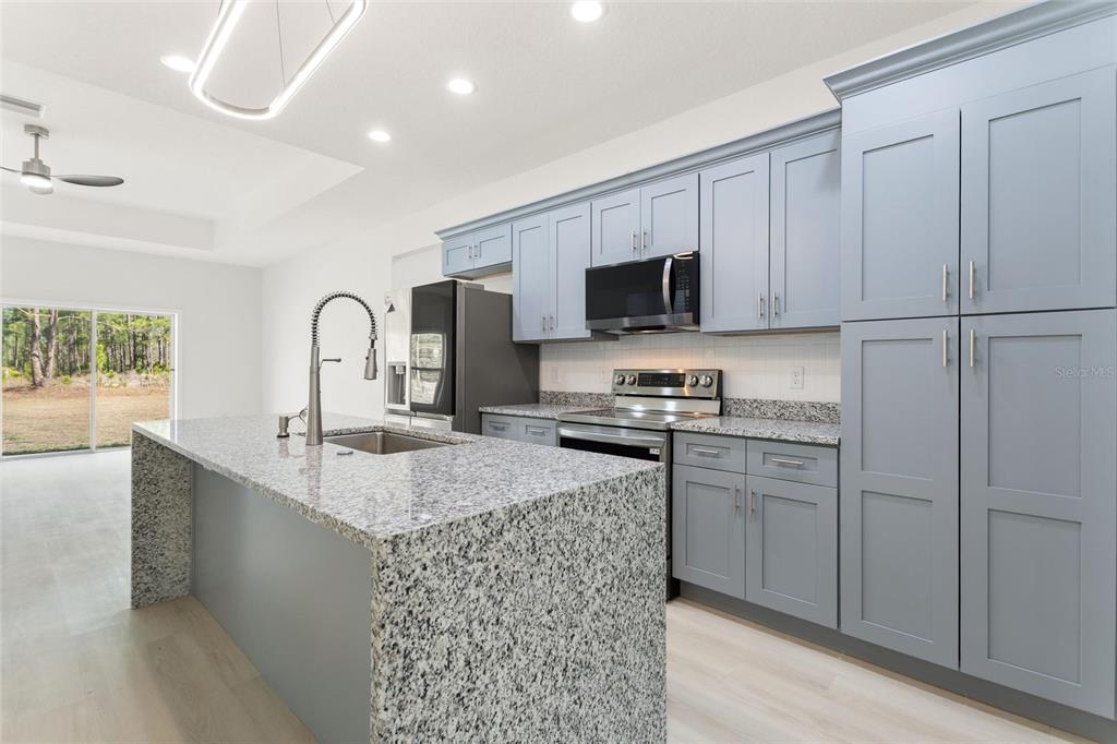 A modern kitchen features light blue cabinets, granite countertops, a large island, and stainless appliances — 3750 JAPONICA AVENUE, INDIAN LAKE ESTATES, FL