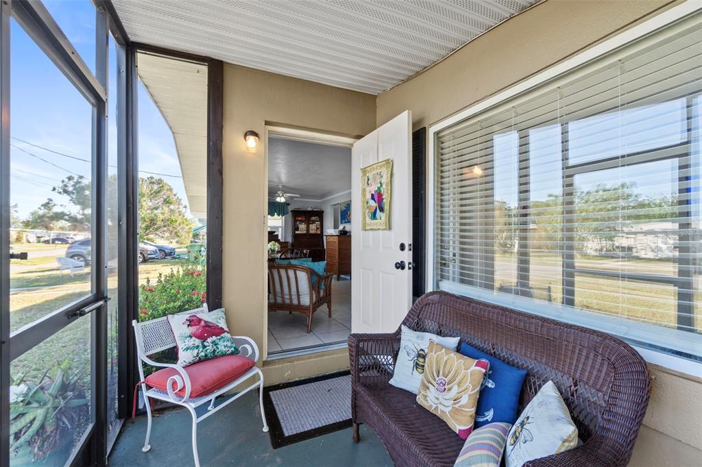 A screened-in porch features a wicker sofa, a white metal chair, and an open doorway — 3197 NORMANDY DRIVE, PORT CHARLOTTE, FL