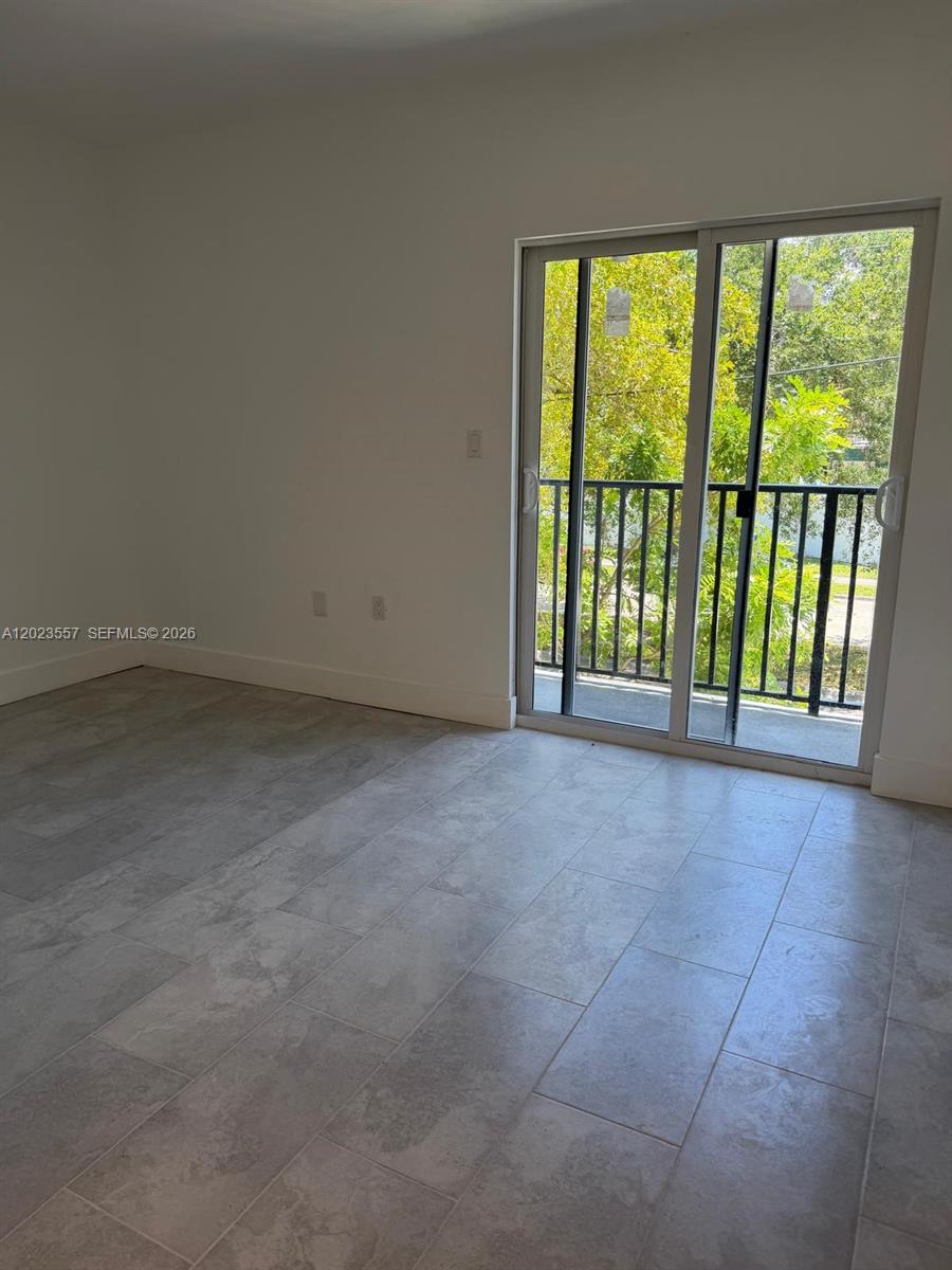 An empty room features light gray tile flooring and a sliding glass door to a balcony — 147 Nw 59th St # 201, Miami FL 33127, MIAMI, FL