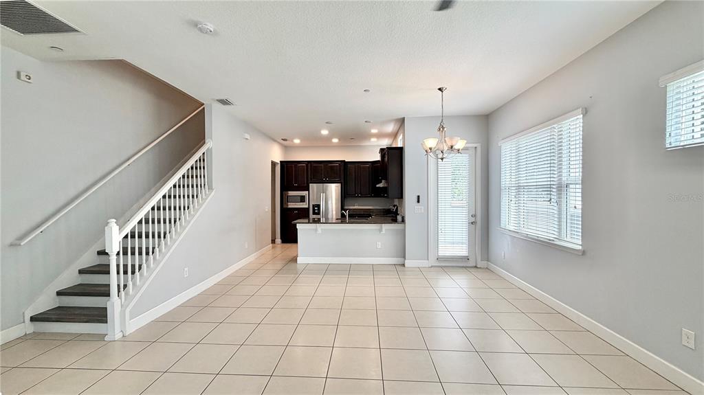 An open-concept living and dining area features tile flooring, a staircase, and a kitchen — 8348 TAVISTOCK LAKES BOULEVARD, ORLANDO, FL