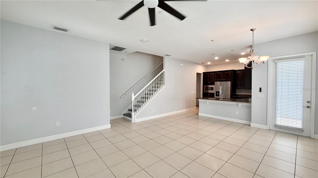 An open-concept living area features tile flooring, a staircase, and a kitchen with dark cabinetry — 8348 TAVISTOCK LAKES BOULEVARD, ORLANDO, FL